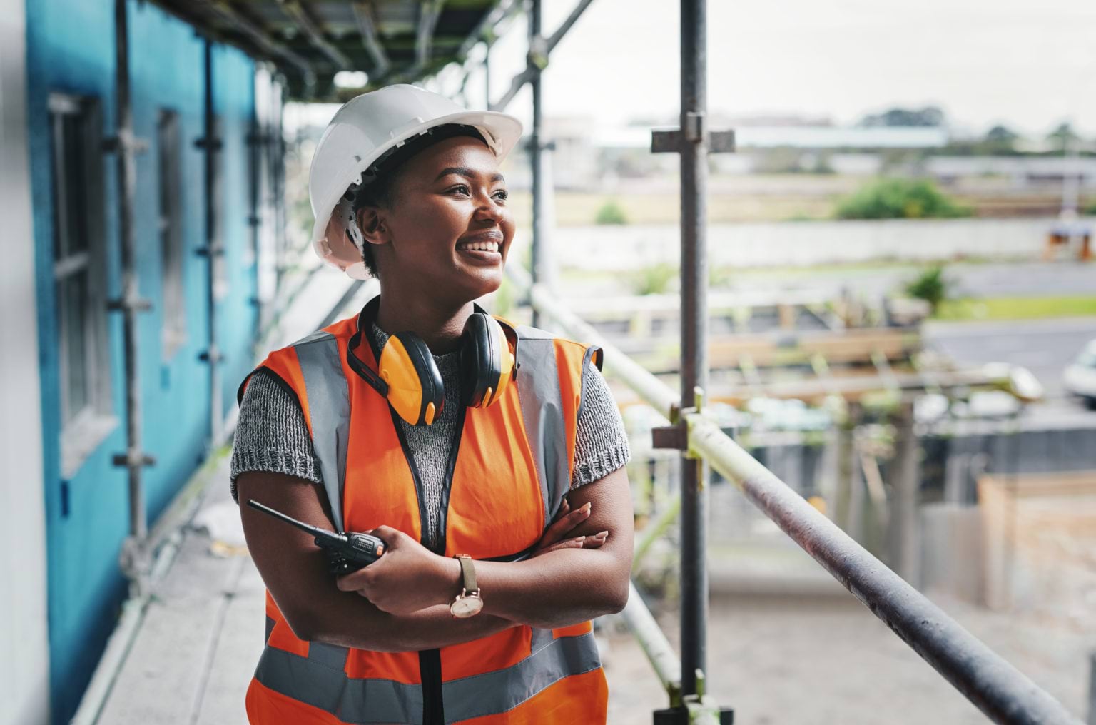 An apprentice, in hardhat and high-vis, standing on a scaffold at a building site