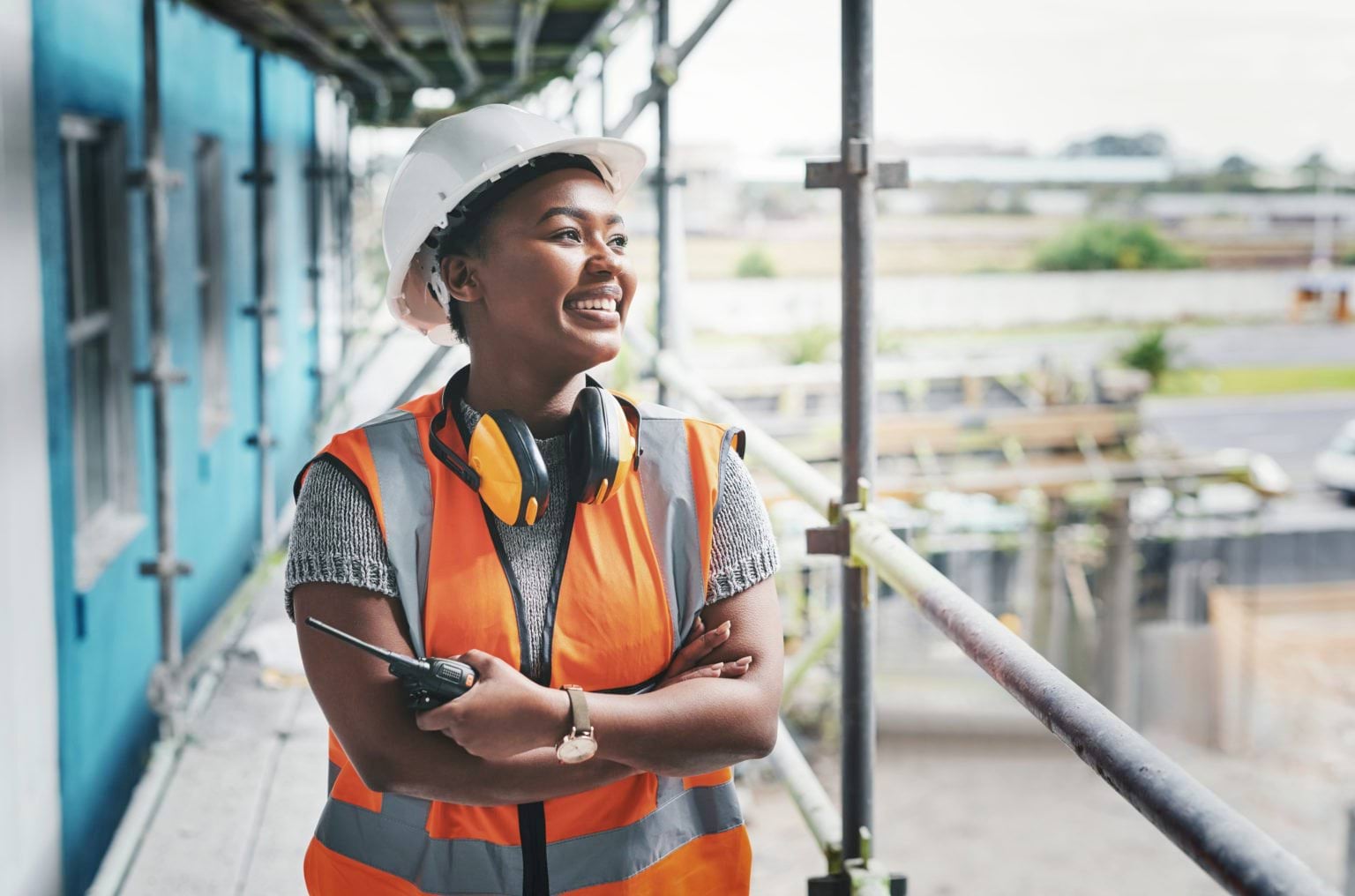 An apprentice, in hardhat and high-vis, standing on a scaffold at a building site