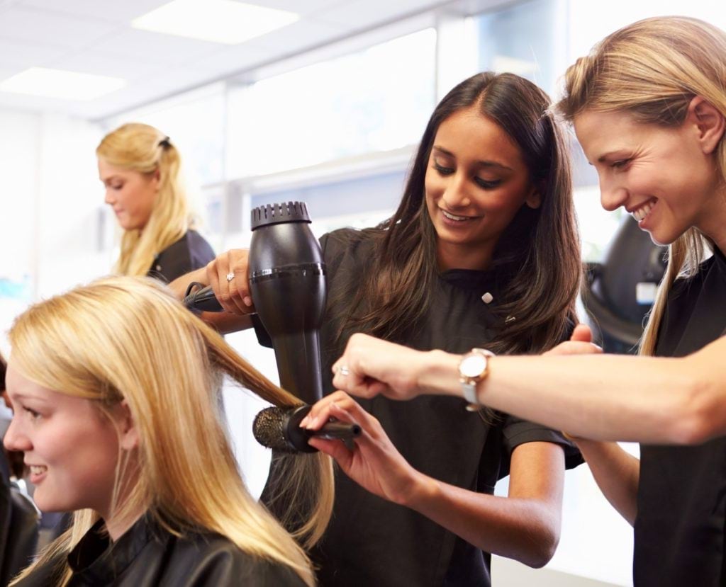 Apprentice hairdressers practicing styling another apprentice's hair