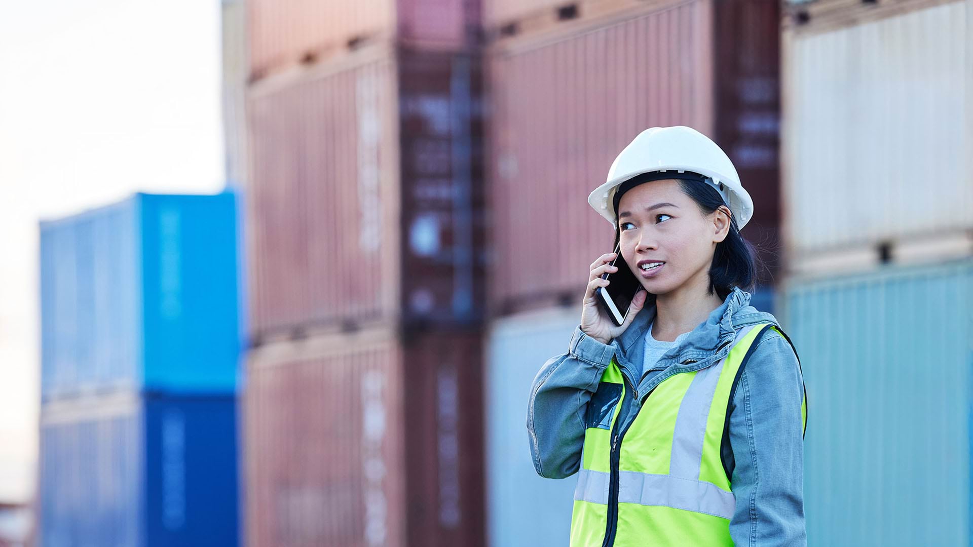 Apprentice wearing hard hat and high-vis vest, speaking on mobile phone